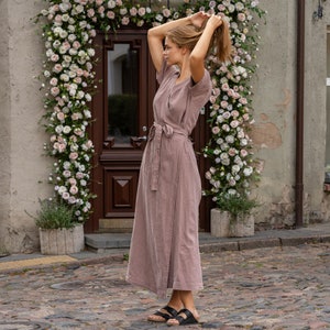 The model wears the ELEANOR maxi wrap dress in faded rose. She is standing full height sideways to the camera, revealing the dress in full length. She is holding up her hair.