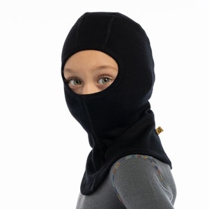 May include: Black balaclava made of wool with a hole for the eyes. The balaclava is worn by a child.