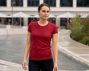 Può includere: Una donna indossa una maglietta rossa a maniche corte e pantaloni neri e cammina all'aperto.