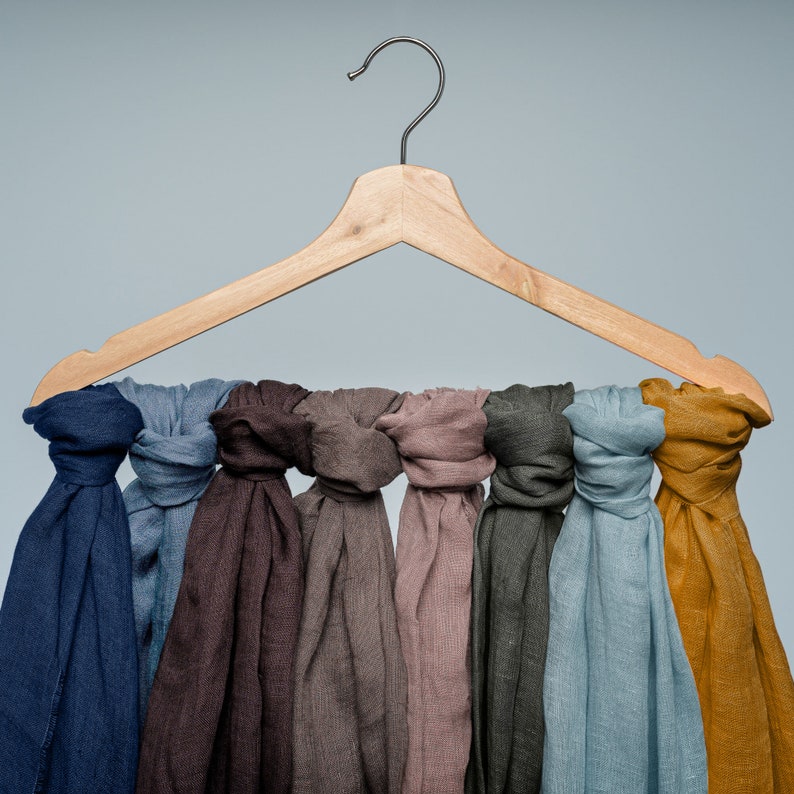 May include: A wooden hanger with eight different colored scarves hanging from it. The scarves are in shades of blue, brown, gray, and yellow.