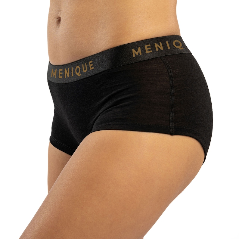 K&ouml;nnte beinhalten: Schwarze Unterw&auml;sche mit einem breiten elastischen Bund, auf dem "MENIQUE" in goldenen Buchstaben steht.