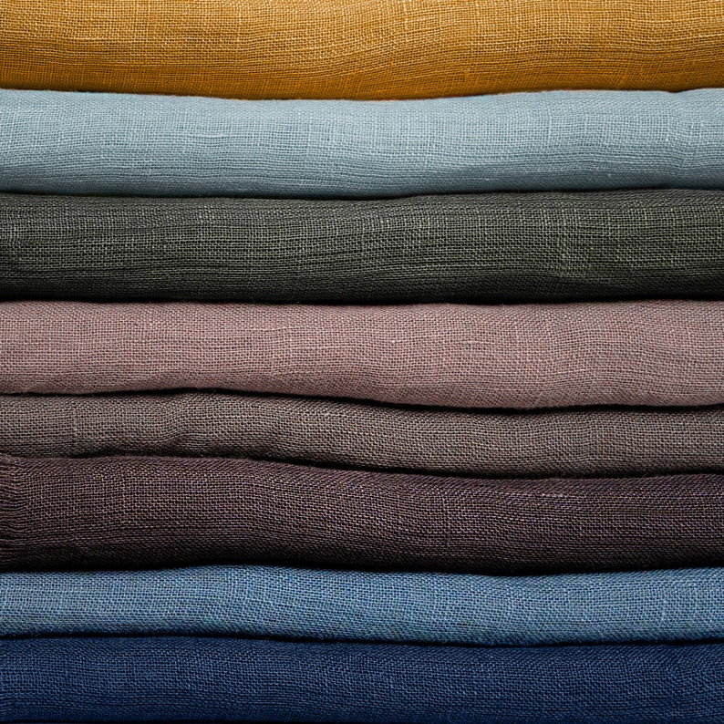 May include: A stack of fabric swatches in various colors, including mustard yellow, light blue, dark gray, mauve, brown, blue, and navy blue. The fabric has a linen texture.