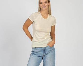 May include: A woman wearing a light yellow short-sleeved t-shirt and blue jeans.