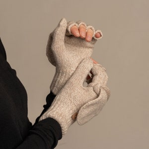 May include: A pair of beige fingerless gloves with a fold-over mitten flap. The gloves are made of a soft, knitted fabric.