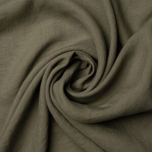 Pu&ograve; includere: Primo piano di un tessuto morbido di colore verde con una texture stropicciata. Il tessuto &egrave; piegato e drappeggiato, creando una curva liscia e fluida.