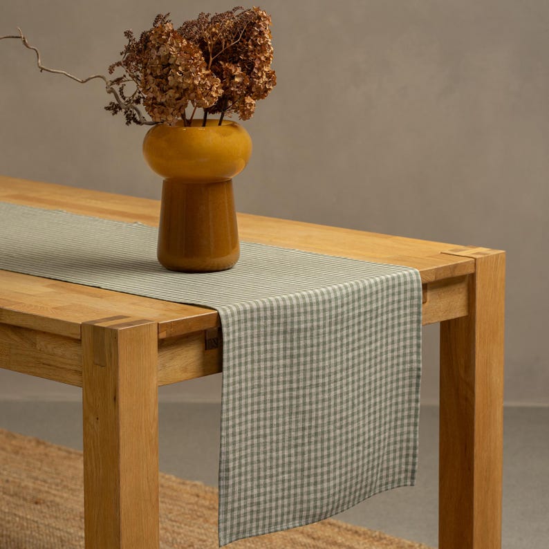 The menique green check color linen table runner on top of a wooden table. There is a vase on top of the runner.