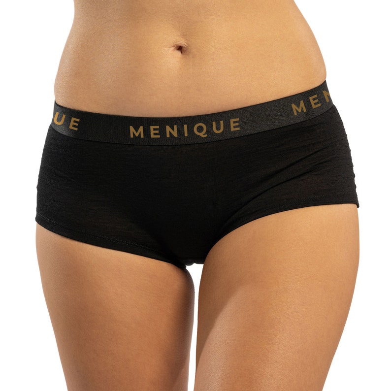 K&ouml;nnte beinhalten: Schwarze Unterw&auml;sche mit einem breiten elastischen Bund, auf dem "MENIQUE" in goldenen Buchstaben steht.