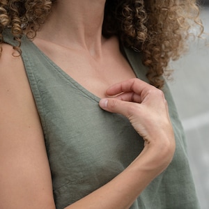 Thispicturefeaturesthe round neckline of the ANA crop top in stone green. The model is touching the neckline with her hand.
