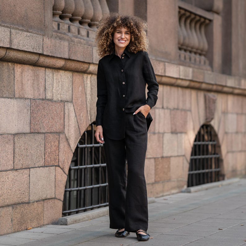 May include: A woman wearing a black linen shirt and matching pants. The shirt has a button-down collar and long sleeves. The pants are wide-legged and have a relaxed fit.