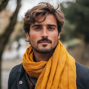 May include: A man with brown hair and a beard is wearing a yellow scarf. He is looking directly at the camera.