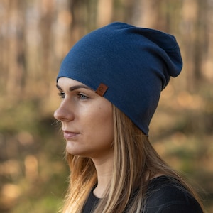 May include: A woman wearing a blue beanie with a brown leather tag. The beanie is slouchy and has a simple design.