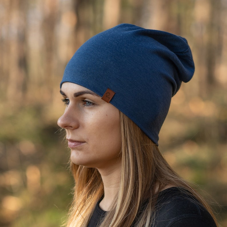 May include: A woman wearing a blue beanie with a brown leather tag. The beanie is slouchy and has a simple design.
