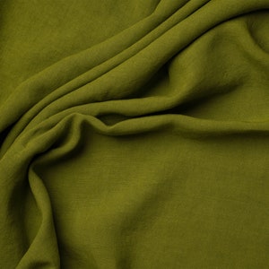 May include: A close-up of a soft, green fabric with a wrinkled texture. The fabric is folded and draped, creating a smooth, flowing surface.