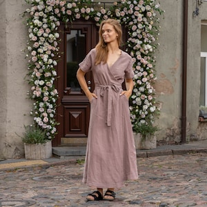 The model wears the ELEANOR maxi wrap dress in faded rose. She is standing full height, with her hands in the side pockets. The wrap design features a v-neck and a belt around the waist.