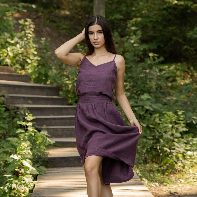 The model is wearing the SOPHIA skirt in shadow purple. She is looking at the camera, with her hand behind her head, the other holding a side of her skirt. The skirt has a wide waist, and is matched with a same color slip top, tucked into the skirt.