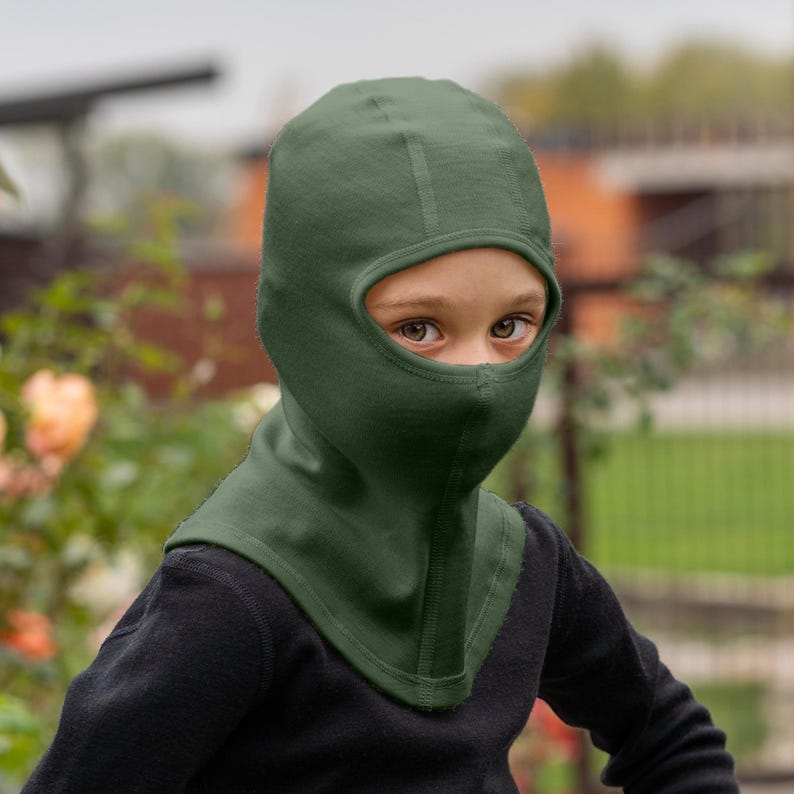 Child wearing a dark green balaclava outdoors with blurred background