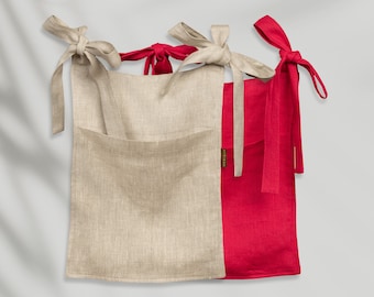 May include: Two linen tote bags, one beige and one red. The beige bag has a pocket on the front and both bags have long ties.