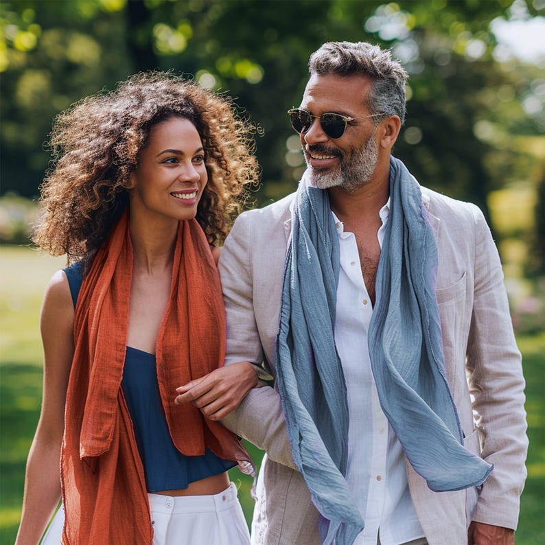 May include: A couple walking outdoors in a park. The woman is wearing a red scarf and a blue top. The man is wearing a light beige blazer with a blue scarf and a white shirt.