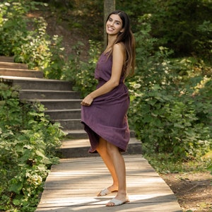 The model is wearing the SOPHIA skirt in shadow purple. She is looking at the camera, smiling, standing sideways. Holding the side of the skirt, she is moving it. This highlights the comfortable shape and midi length of the skirt.