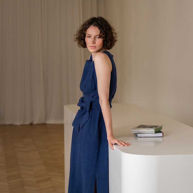 Photograph features a woman wearing the HAILEY summer wrap dress in storm blue color. The woman is leaning on a tabletop. The sideview of the picture accentuates the waist.