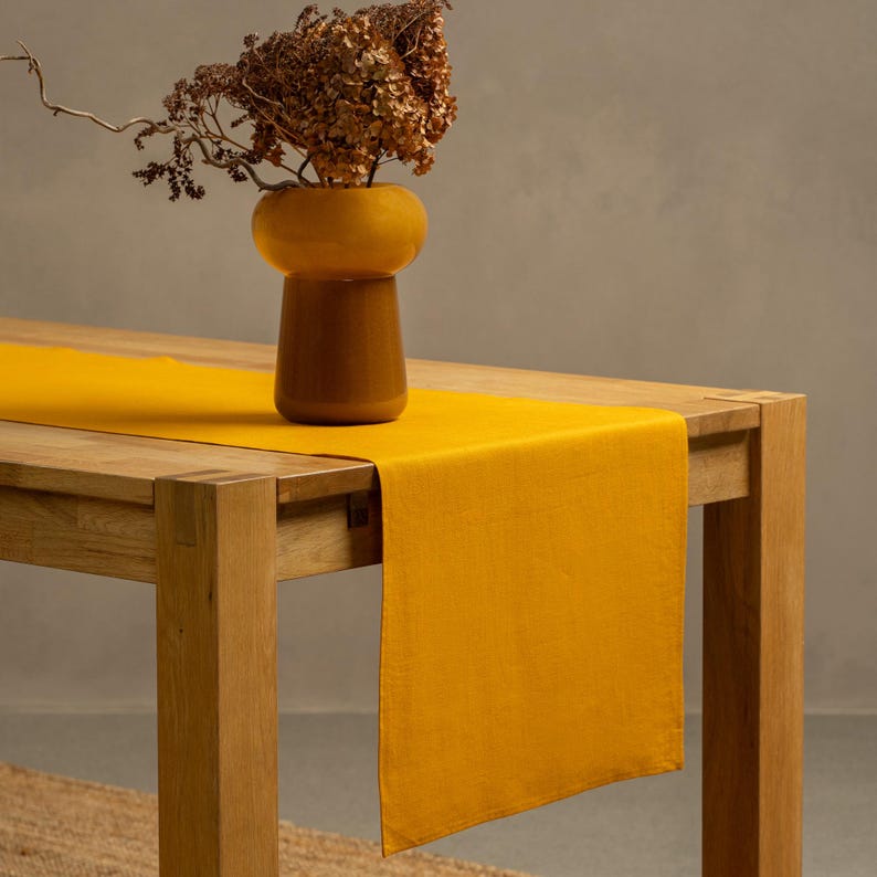 The menique spicy yellow color linen table runner on top of a wooden table. There is a vase on top of the runner.