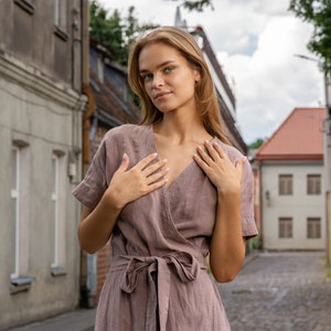 The model wears the ELEANOR maxi wrap dress in faded rose. This is a close-up shot, in which the model is touching the neckline with her hands, highlighting the v form.