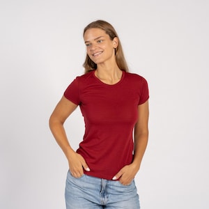 Woman wearing a merino wool menique royal cherry t-shirt and denim jeans standing in white background.