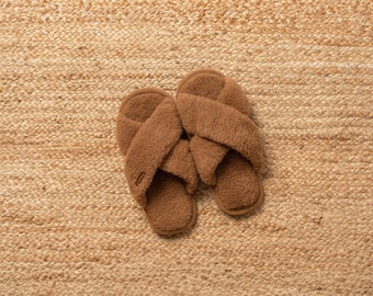 May include: A pair of brown fuzzy slippers with a criss-cross strap design. The slippers are on a woven jute rug.