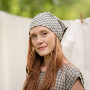 May include: A woman with long red hair wearing a green and white gingham dress and a matching gingham headscarf.