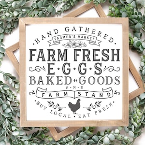 May include: A framed sign with the text "Farm Fresh Eggs & Baked Goods" in a rustic style. The sign is surrounded by greenery and includes a small illustration of a chicken. The words "Farmer's Market" are also included.