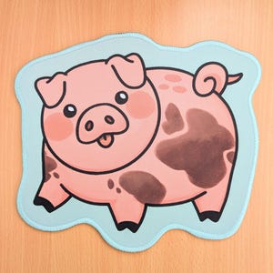 Puede incluir: Un parche de cerdo de dibujos animados rosa con manchas marrones y un borde azul claro. El cerdo tiene una expresión sonriente con la lengua fuera. El parche es probablemente para ropa o accesorios.