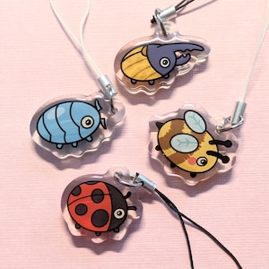 Pode incluir: Quatro amuletos de insetos diferentes em chaveiros transparentes. Os amuletos são um bicho-de-conta azul, um besouro amarelo e castanho, uma abelha amarela e castanha e uma joaninha vermelha.