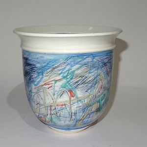 Könnte beinhalten: Ein weißer Keramiktopf mit einem abstrakten Design in Blau, Grün und Gelb. Der Topf hat einen breiten, abgerundeten Boden und einen leicht ausgestellten Rand.