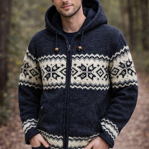 May include: A navy blue hooded zip-up sweater with a cream and black geometric pattern. The sweater has a drawstring hood and wooden toggles. The person is wearing blue jeans and has their hands in their pockets.