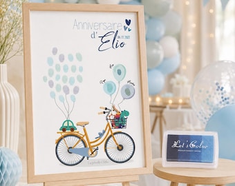 May include: A framed print featuring a yellow bicycle illustration with a basket and rear rack, decorated with blue and purple fingerprint balloons. The text reads Anniversaire d'Elio 06 01 2022. A blue ink pad is placed on a small wooden stool nearby.