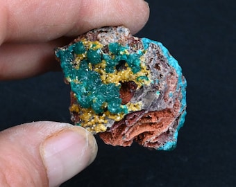 Puede incluir: Un primer plano de una muestra mineral verde, amarilla y marrón. La muestra tiene una superficie rugosa y texturizada y está cubierta de pequeños cristales.