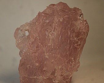 May include: A large, pink, translucent crystal with a rough, irregular surface. The crystal has a natural, raw appearance.