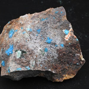 Puede incluir: Una roca marrón oscura y rugosa con manchas dispersas de depósitos minerales azul brillante y blanco.