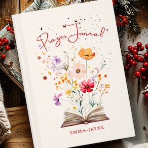 May include: A white prayer journal with a floral illustration featuring an open book with colourful wildflowers growing from the pages. The text Prayer Journal is written in red script at the top, and the name EMMA-JAYNE is printed in red at the bottom.