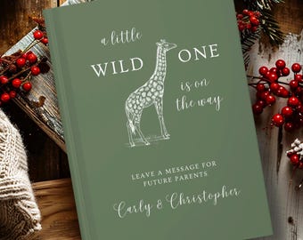 May include: A sage green hardcover guest book featuring a white line drawing of a giraffe. The text reads: a little WILD ONE is on the way, LEAVE A MESSAGE FOR FUTURE PARENTS, and the names Carly & Christopher in a script font.