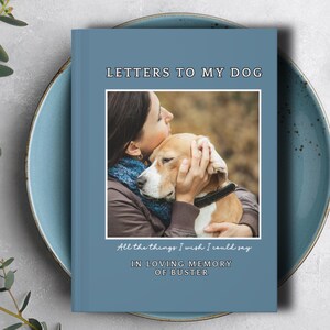 May include: A blue journal titled "LETTERS TO MY DOG" with a photo of a person hugging a dog. The text "All the things I wish I could say" and "IN LOVING MEMORY OF BUSTER" are also on the cover. The journal is on a blue plate.