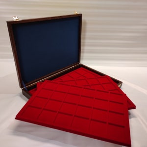 Puede incluir: Una caja de colección de monedas de madera con un acabado marrón oscuro y un interior de terciopelo azul. La caja tiene tres bandejas de terciopelo rojo con compartimentos para guardar monedas.