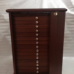 Puede incluir: Un armario de madera oscura con una puerta con bisagras y 12 cajones. Cada cajón tiene una perilla de latón. El armario es ideal para guardar objetos pequeños.