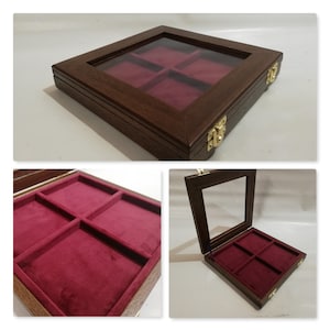 Puede incluir: Una caja de madera con tapa de vidrio y cuatro compartimentos forrados con terciopelo rojo. La caja tiene bisagras y cierres de latón.