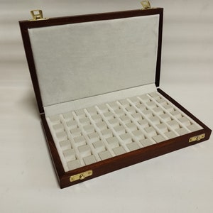 Puede incluir: Una caja de madera con tapa abatible y un interior de terciopelo blanco. La caja tiene 60 compartimentos para guardar objetos pequeños, como anillos, pendientes u otras joyas.