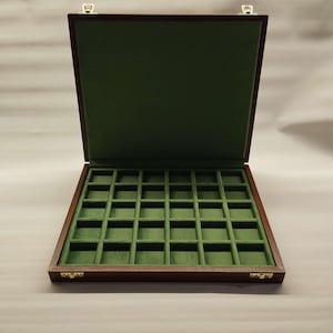 以下が含まれることがあります： 濃い茶色の外装と緑色のベルベットの内装の木製ディスプレイケース。ケースは開いており、複数の正方形のコンパートメントが明らかになっています。蓋も緑色のベルベットで裏打ちされています。ケースには金色の留め金が付いています。