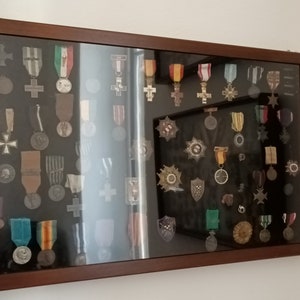 May include: A framed display case with a black background showcasing a collection of military medals and ribbons. The medals are arranged in rows and columns, and they are of various sizes and colors. The case is made of wood and has a glass front.