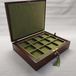 May include: A wooden jewelry box with a hinged lid, open to reveal a green velvet interior and compartments. The box is rectangular with a dark brown finish, a gold-colored clasp, and a green tassel.
