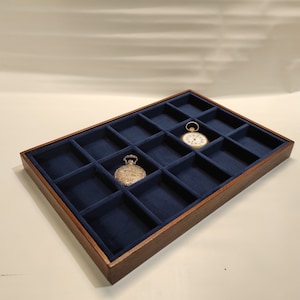 Può includere: Una scatola di presentazione per orologi in legno con 16 scomparti rivestiti in velluto blu. Due orologi da tasca sono esposti nella scatola.