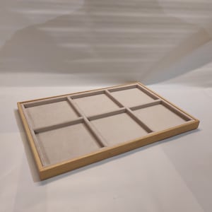 Può includere: Un vassoio in legno con sei scomparti rivestiti in feltro grigio chiaro. Il vassoio è realizzato in legno naturale e ha un colore marrone chiaro.